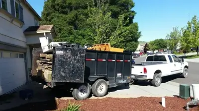 Junk removal truck loaded with items next to a driveway.