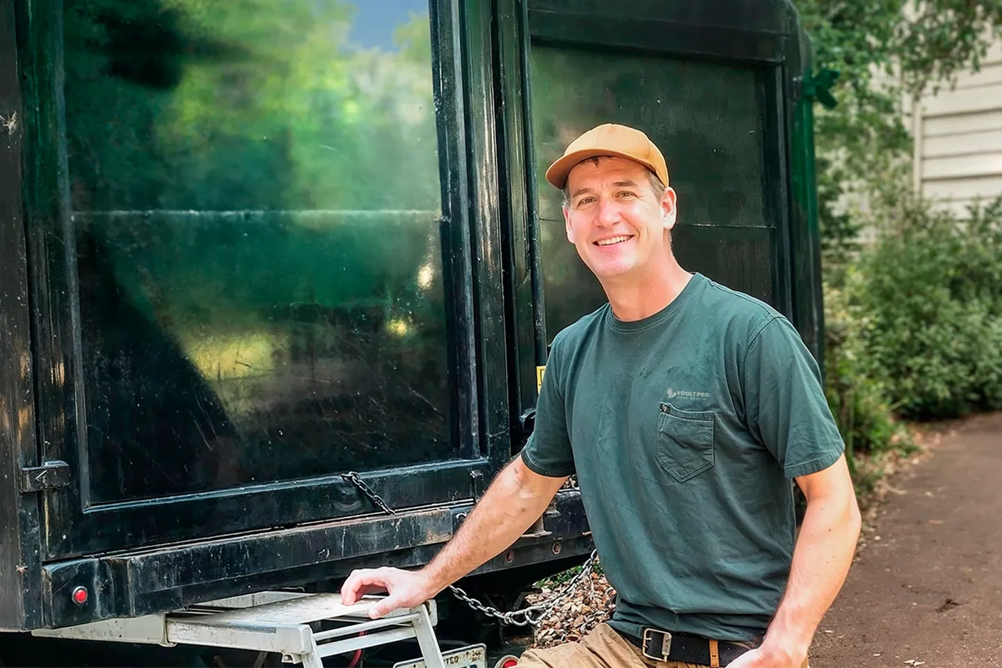A smiling VooltPro Junk Removal employee standing behind a truck ready to haul away junk|.